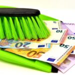 Contanti nascosti sotto un materasso con una mano che li esamina, simbolo di risparmio e evasione fiscale.